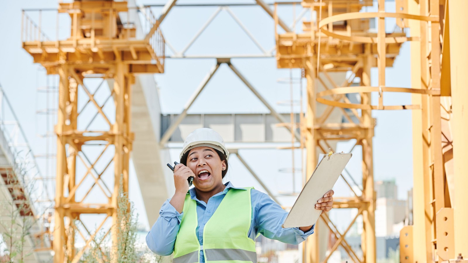 Female construction worker using a radio and clipboard to report a site issue.